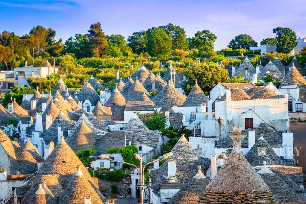 luxury Apulia tour, Baroque architecture facade of Basilica di Santa Croce in Lecce Southern Italy with intricate limestone carvings, Golden baroque buildings and elegant piazza in historic Lecce Puglia Italy at sunset, Traditional white trulli houses with cone-shaped roofs in Alberobello UNESCO World Heritage Site, Dramatic clifftop view of Polignano a Mare coastal town perched above turquoise Adriatic Sea, Ancient Sassi cave dwellings carved into limestone cliffs in Matera UNESCO site Italy, Whitewashed buildings and narrow alleyways in hilltop Ostuni white city Puglia, Private luxury catamaran sailing along dramatic coast of Polignano a Mare with sea caves, Panoramic aerial view of Itria Valley showing traditional trulli houses and olive groves Puglia, Historic olive oil estate in Puglia with ancient olive trees and stone farmhouse, Medieval cathedral mosaic floor in Byzantine Otranto showing religious and mythological scenes, Southern Italy vacation, Puglia luxury travel, Lecce tours, trulli houses Alberobello, Matera tours, Polignano a Mare boat tour